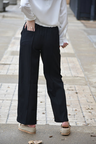 Person wearing black wide-leg pants and a white top on a sidewalk.