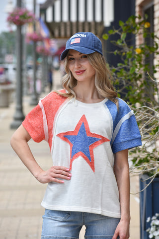 Woman wearing a colorful star-themed shirt and cap outdoors. Good for Memorial Day or 4th of July
