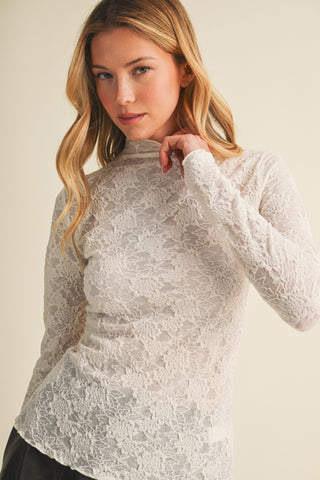 Woman wearing an ivory long sleeve lace mesh top with mock neck